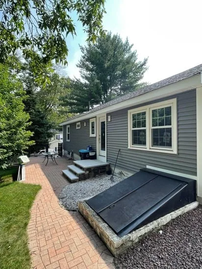 Rear exterior of the house from the Shrewsbury Vinyl Siding Project, showing the new grey siding, the replaced windows and doors, and the integrated dark bulkhead door and brick patio.